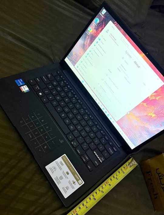 Top-down view of an open ASUS Vivobook 14 laptop, with a yellow tape measure placed alongside the bottom edge of the chassis to verify its physical width dimensions.