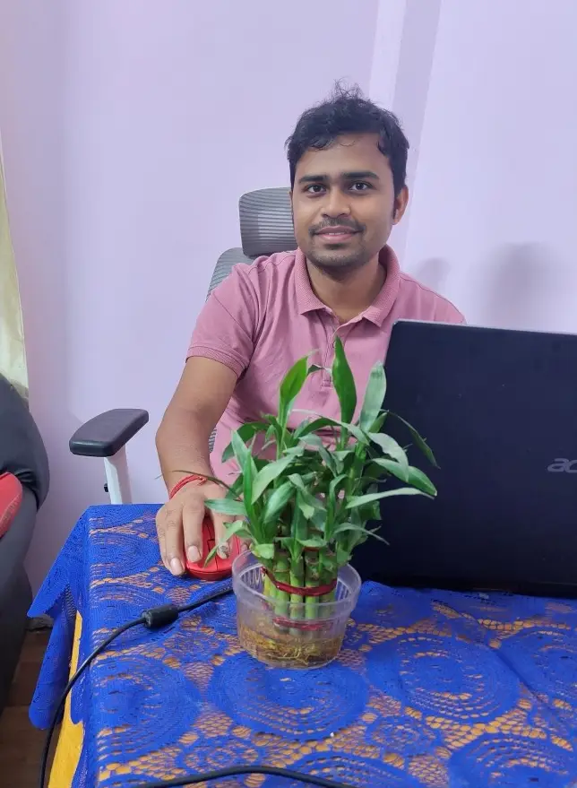 Laptop reviewer Abhishek Roy smiling at his workspace alongside a lucky bamboo plant and his Acer laptop.