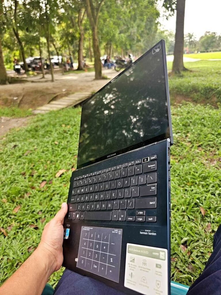 Testing the ASUS Zenbook 14 OLED display panel outdoors, showing the screen's reflection of the park environment to evaluate sunlight visibility.