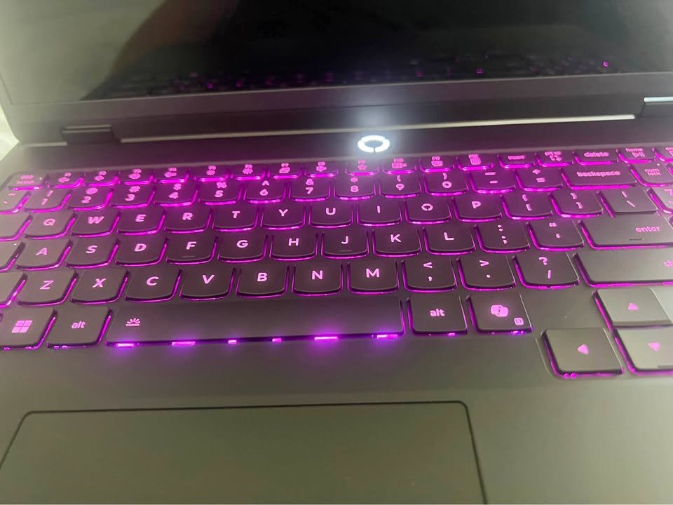 Angled view of an illuminated Lenovo Legion laptop keyboard with pink RGB lighting and a glowing top-center power button.