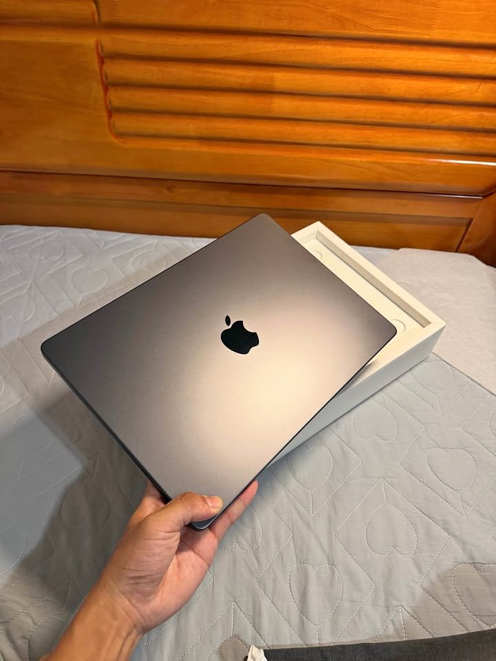 Reviewer holding a newly unboxed Space Gray MacBook Pro in one hand over its open retail box to assess its weight measure and overall portability.